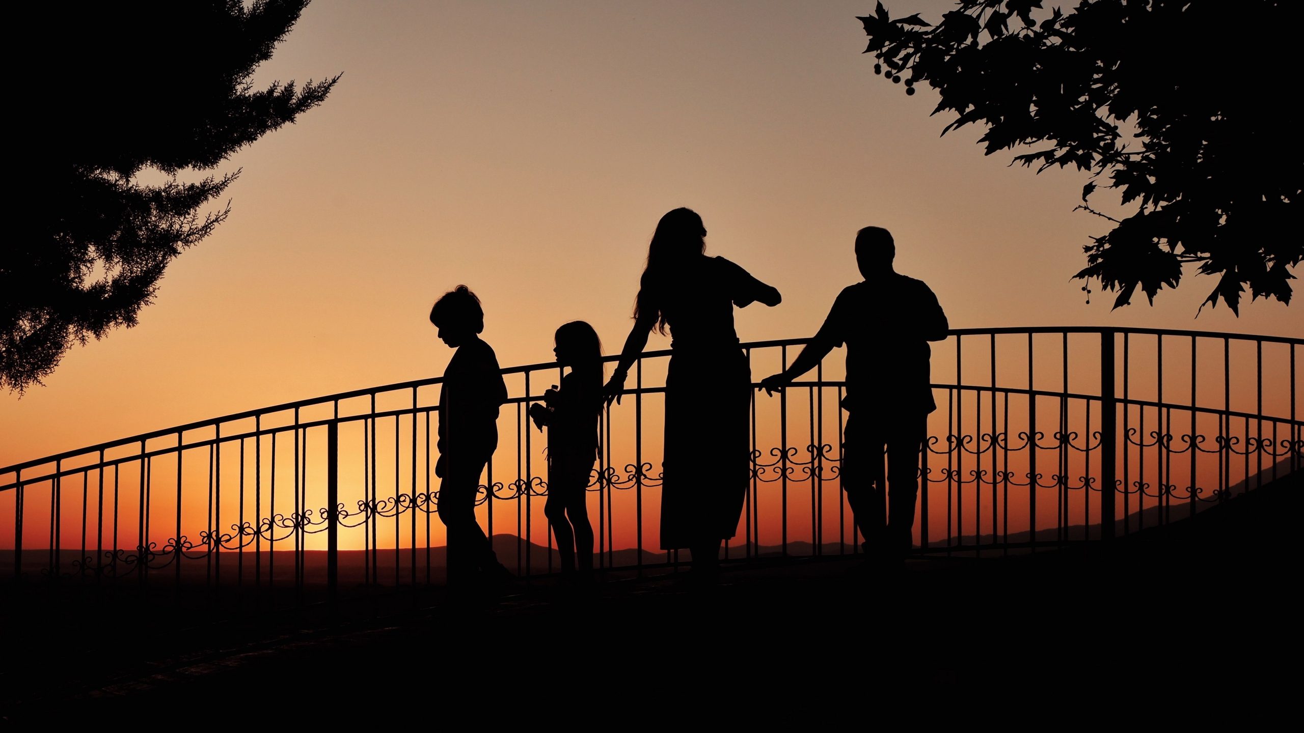 A family enjoying a beautiful sunset silhouetted on a bridge, creating a heartwarming scene.
